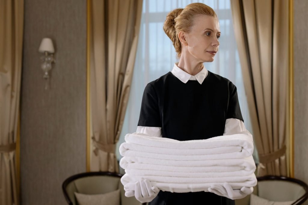 Elegant hotel housekeeper holding fresh, neatly folded white towels in a luxurious room.