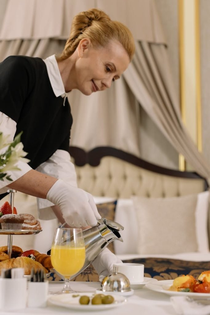Hotel staff serving breakfast with coffee and orange juice in a luxurious room setting.